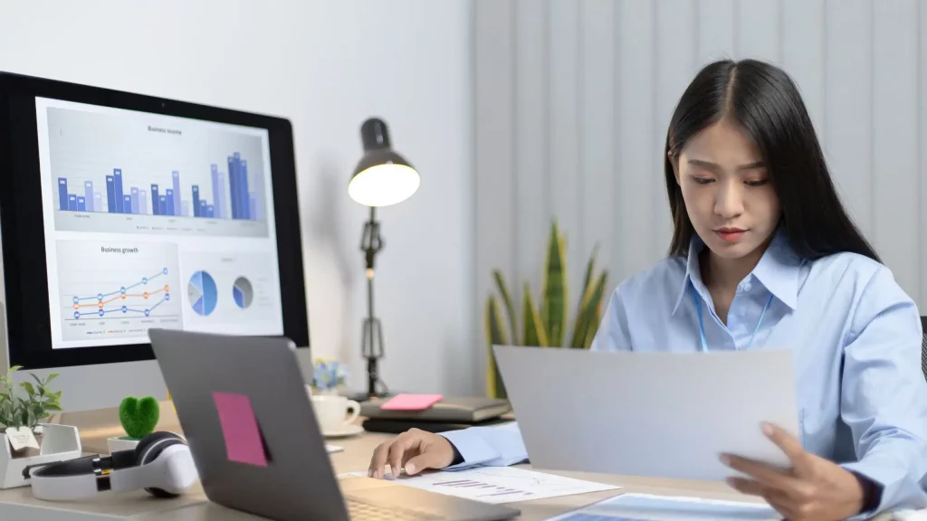 Woman working at desk with laptop open and additional computer screen to the right