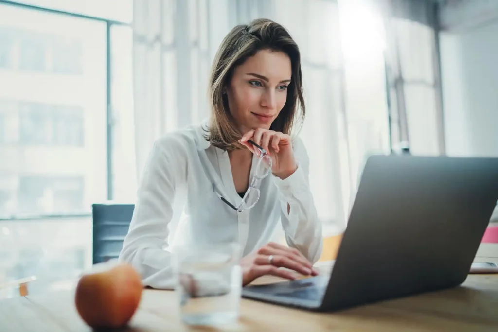 Woman working at desk on laptop with white blouse